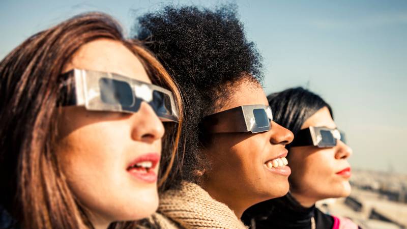 Three women looking at the eclipse wearing eclipse glasses.