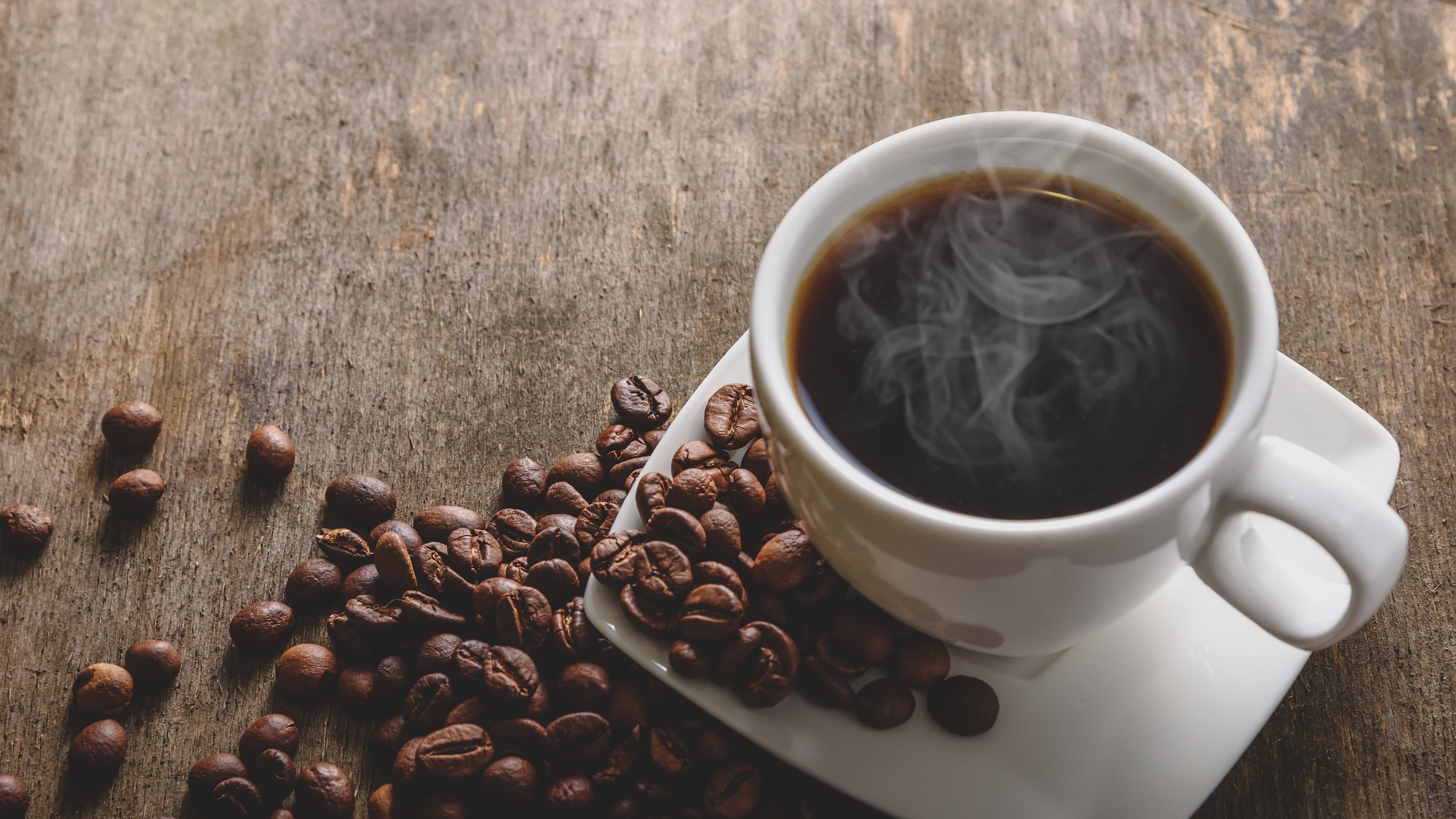 Fragrant hot coffee in a white cup with beans spilling roasted coffee.